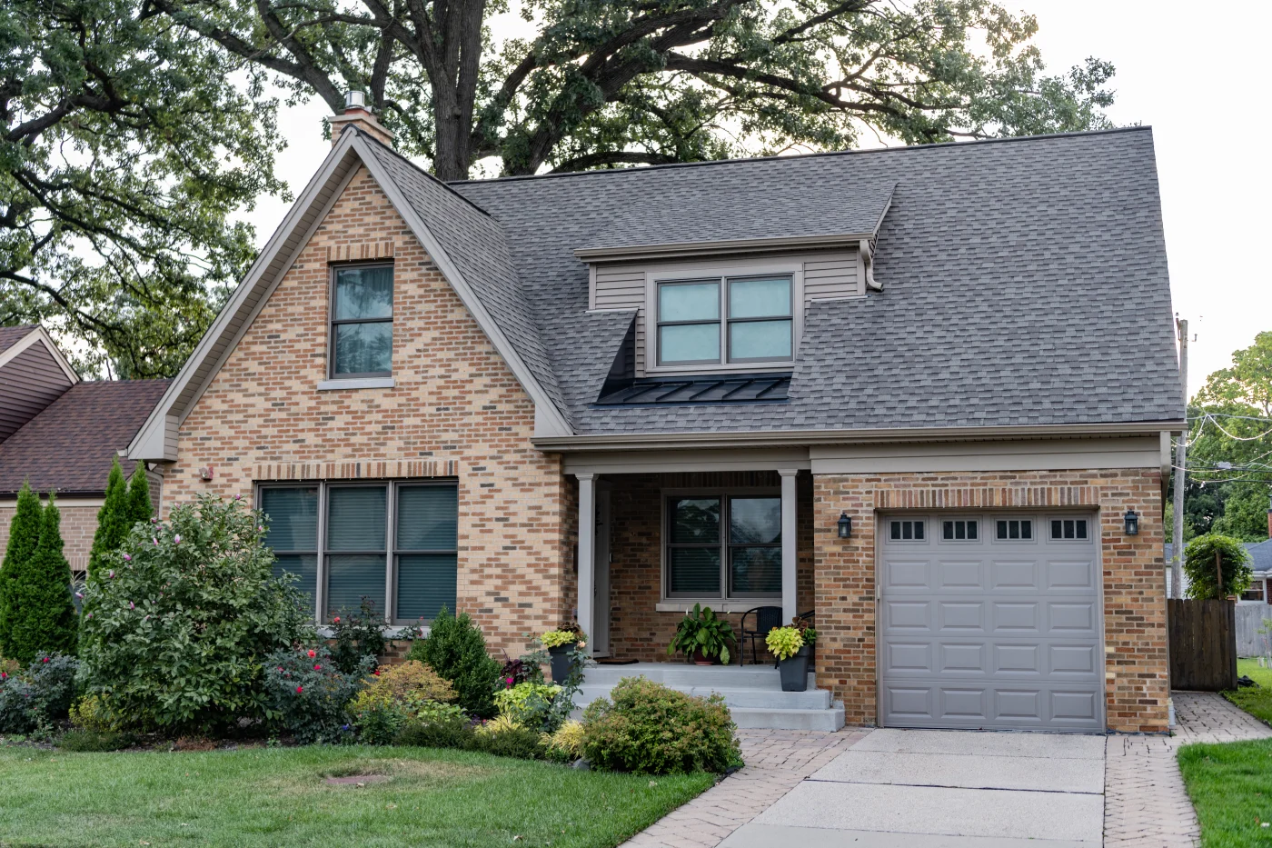 A brick house with a gray garage door, gray trim, gray windows, and an asphalt shingle roof.