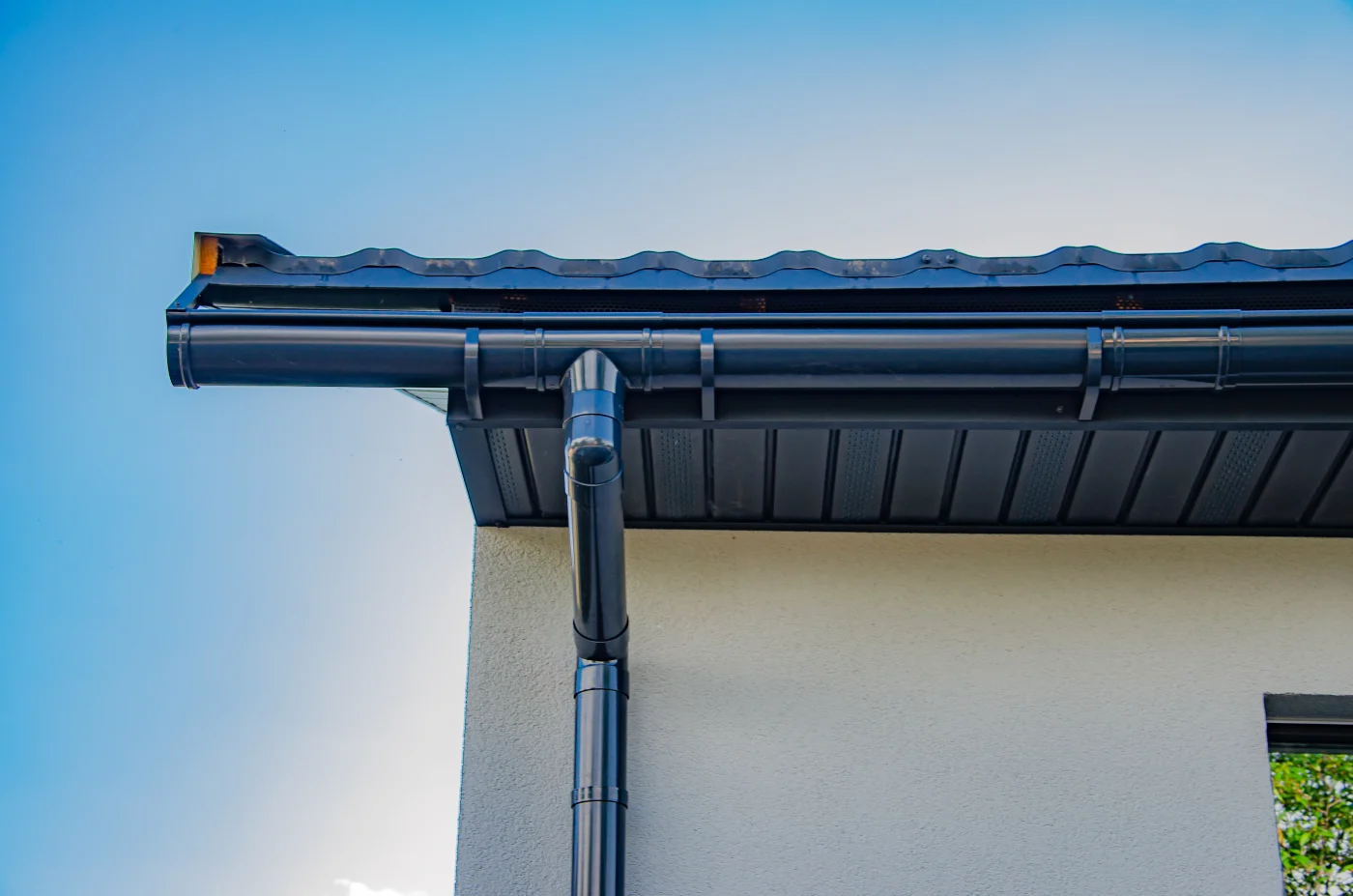 A close-up view of blue gutters and a blue downspout on a stucco house.