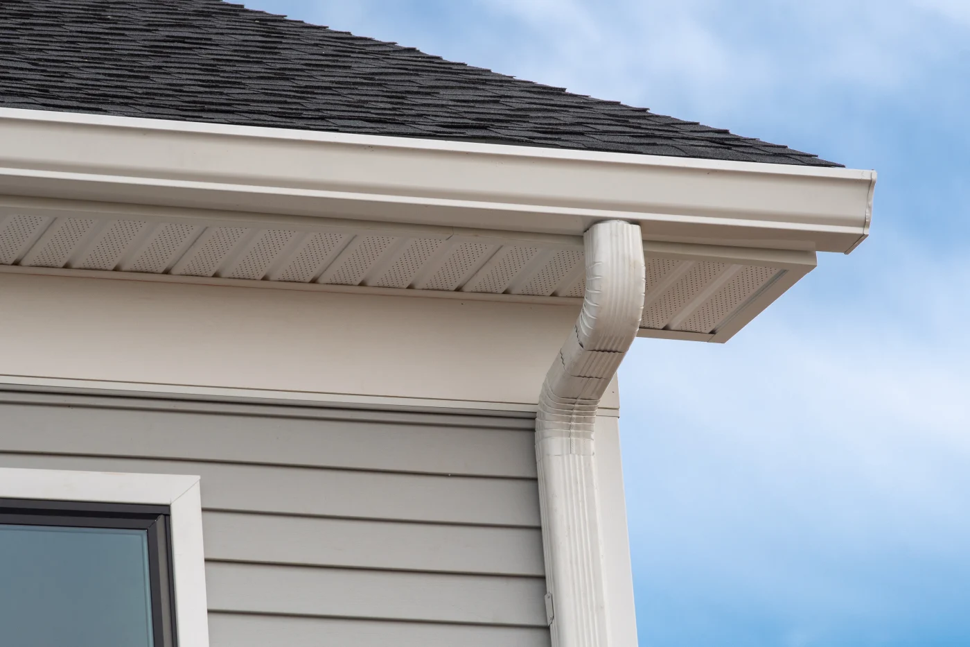 A close-up view of white gutters and a white downspout on a gray house with white trim.
