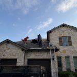Roofers working on an asphalt shingle roof of a stone house