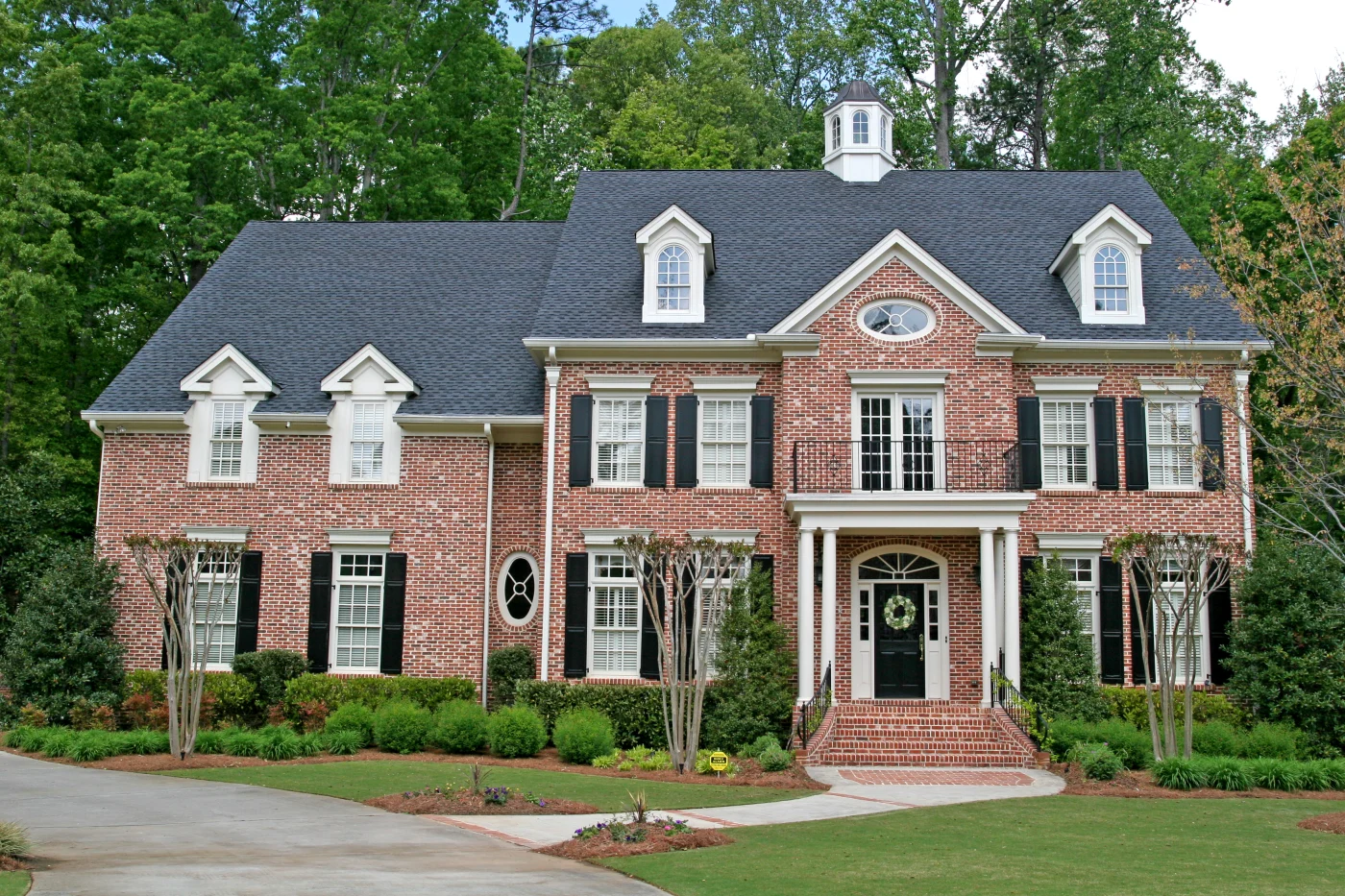 A two-story brick house with tan trim, a black front door, and an asphalt shingle roof.