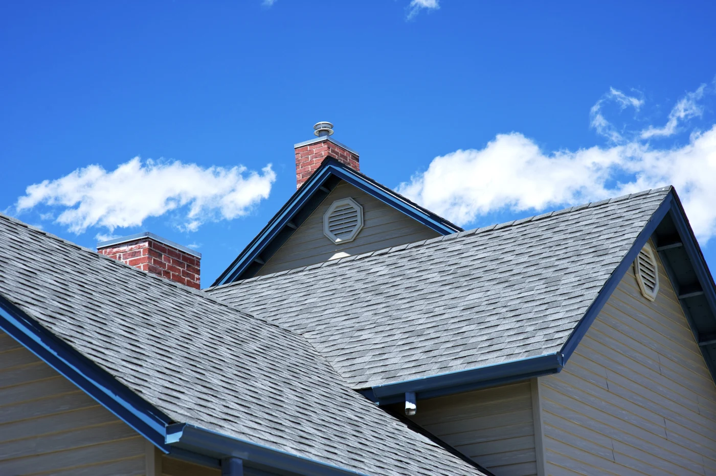 An up-close view of an asphalt shingle roof with blue gutters on a gray house.