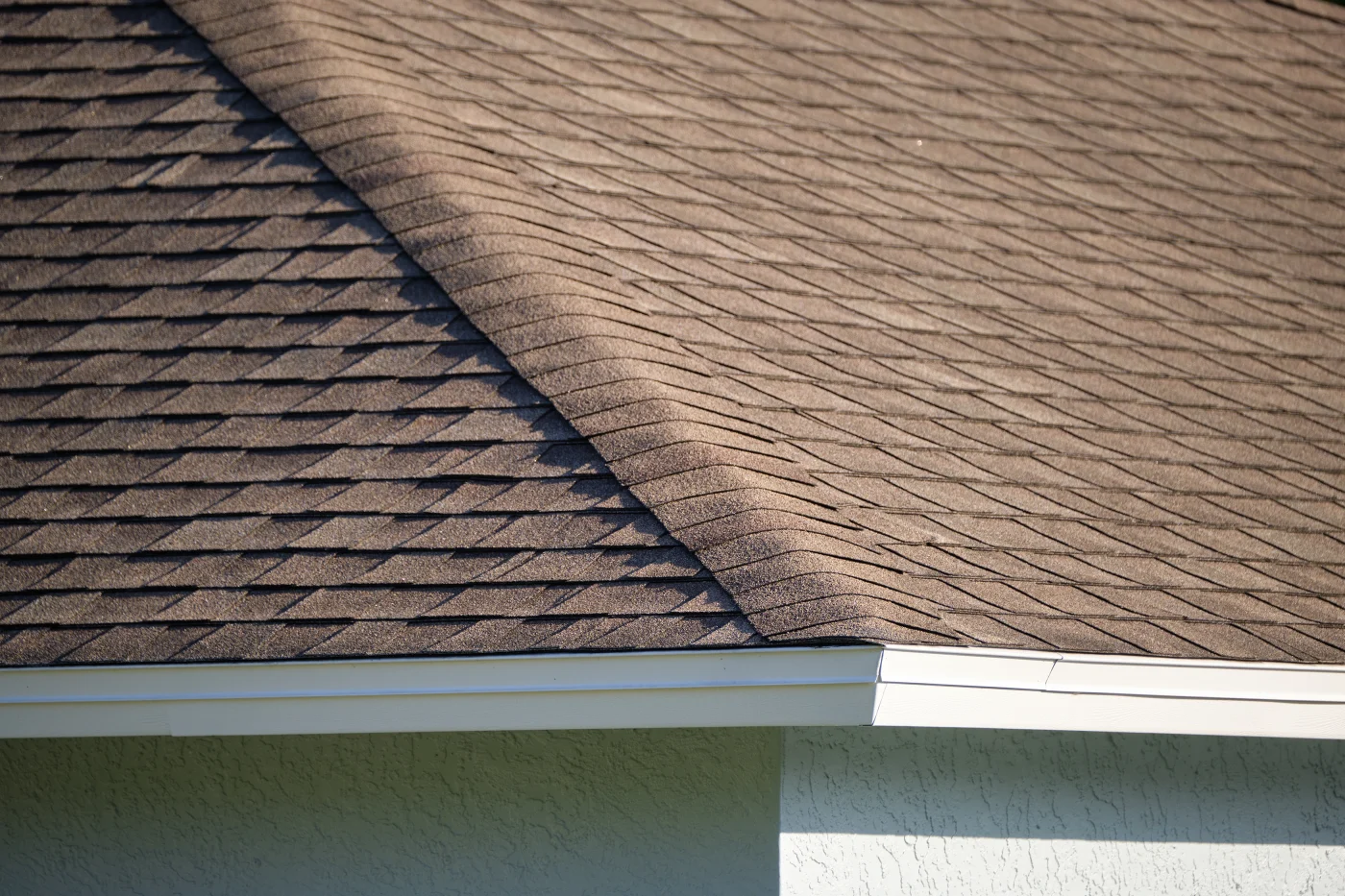 A close-up view of the corner of an asphalt shingle roof on a house with white trim.