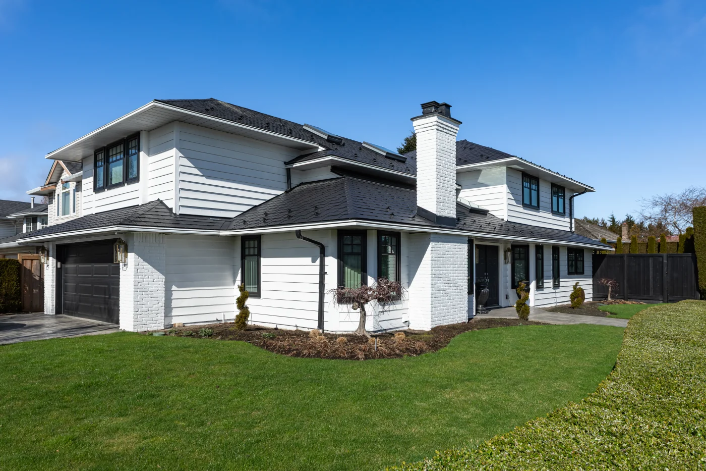 The corner of a two-story white house with black windows, a black garage door, and a metal roof.