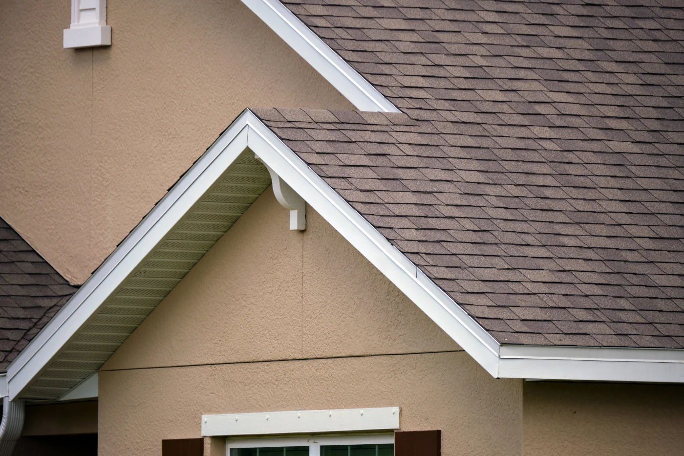 The corner of an asphalt shingle roof with white trim on an orange house.