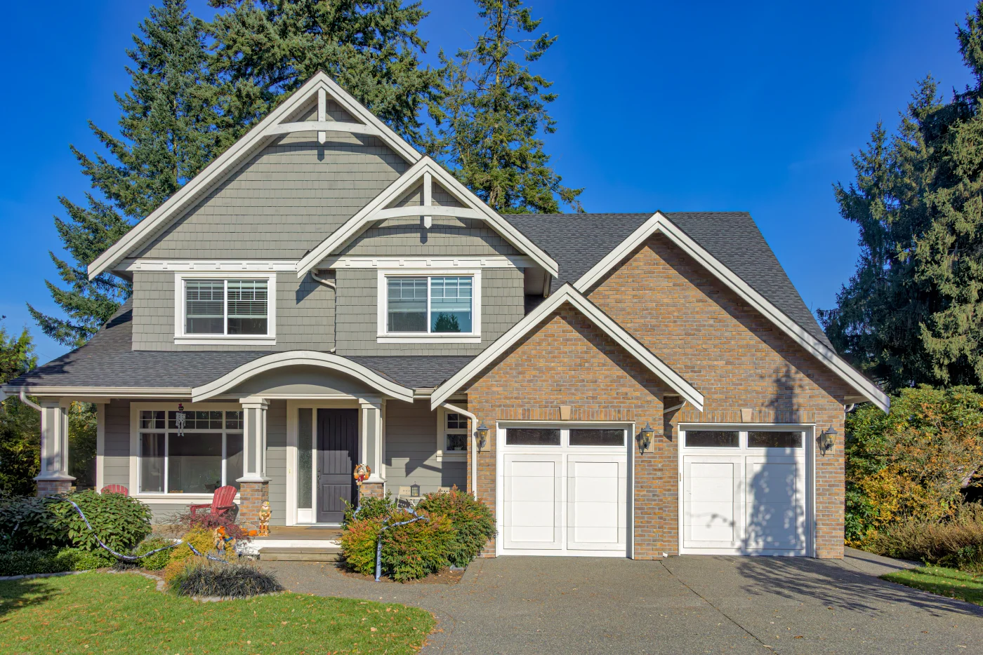 A two-story brick and gray house with two white garage doors, a blue front door, white windows, and an asphalt shingle roof.