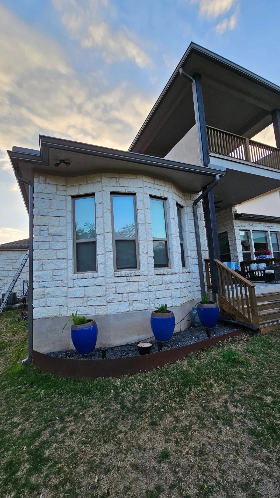 A beautiful stone home features freshly installed dark gutters and downspouts along the roofline, showcasing the precise detail work of a professional roofing company.
