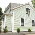 A charming two-story home showcases a fresh coat of light green siding paint paired with clean white trim and black window frames from a professional exterior painting project.