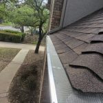 A professional gutter installation project features a clean, seamless aluminum gutter with protective mesh guards along an asphalt shingle roofline