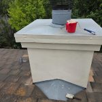 A freshly painted chimney structure on a tiled roof sits alongside a paint roller and brush used during a professional home exterior repair project.