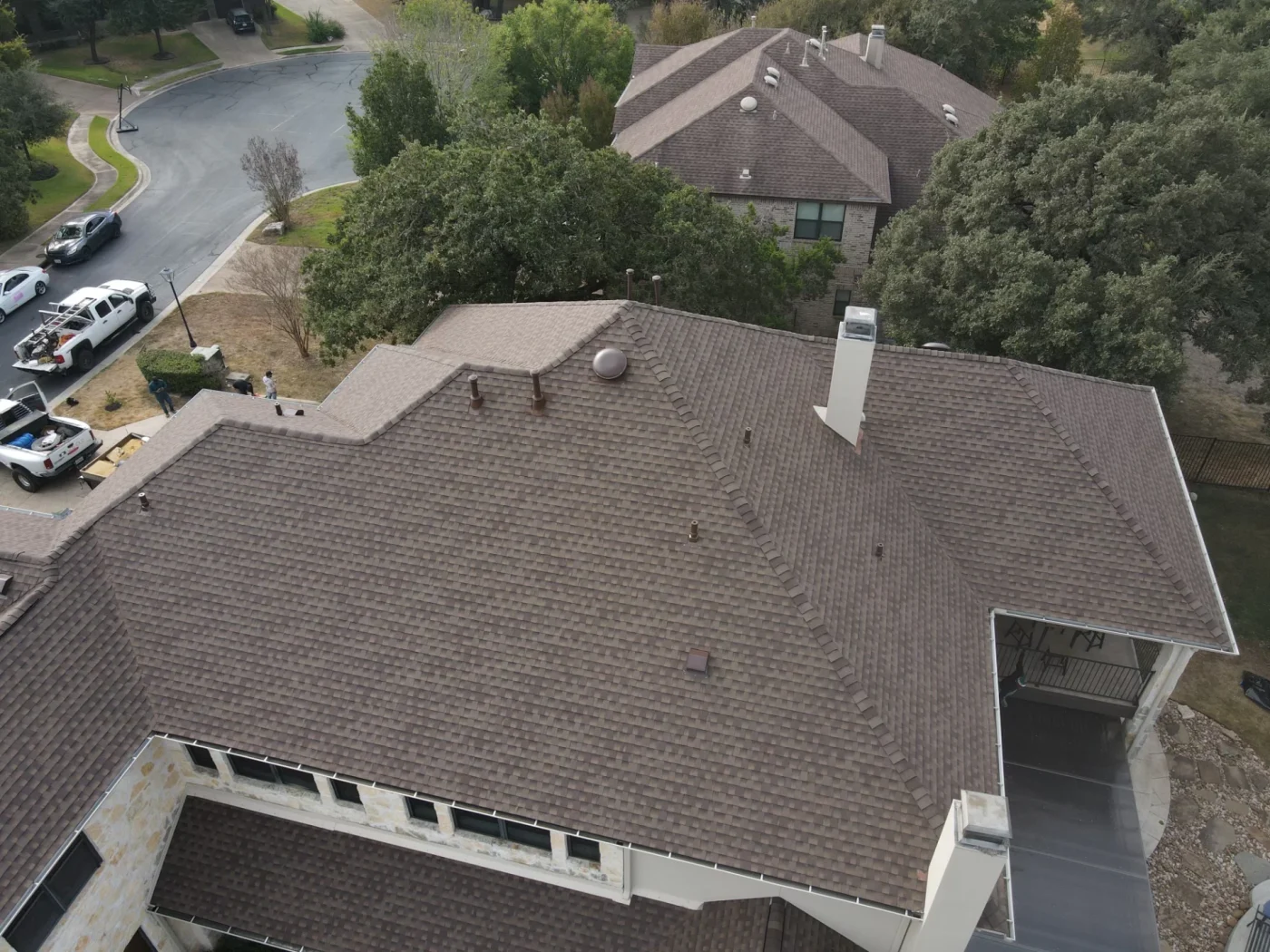 An aerial view of an asphalt shingle roof on a stone and stucco house.
