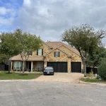 A tan stucco house with a stone base undergoing a stucco repair with a contractor working on the stucco.