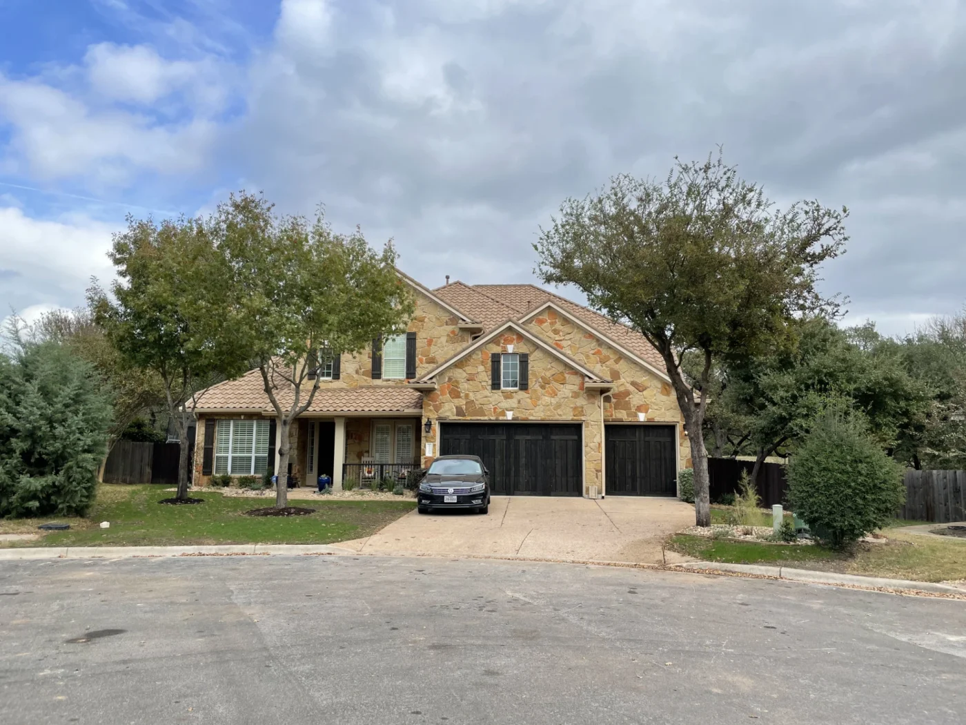 Durable Tile Roofing Austin Tx Wolfpack Roofing And Exteriors A stone house with a front porch, white windows, black shutters, and a tile roof.