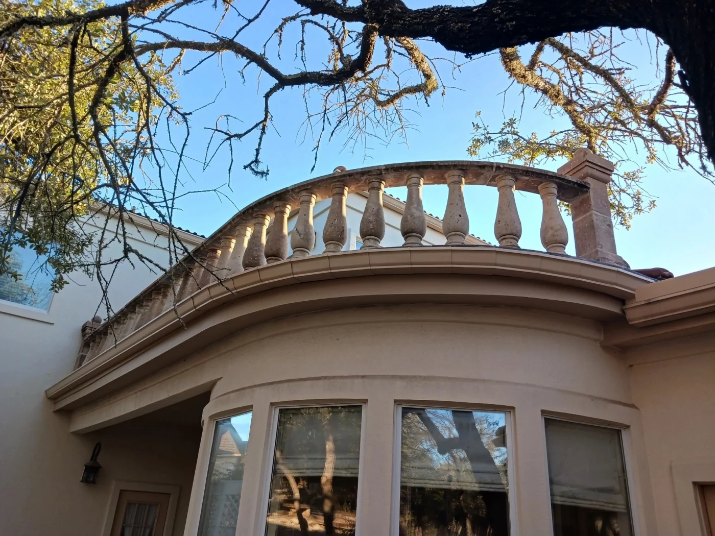 Looking up at a residential stone home reveals a curved upper balcony with a detailed stone balustrade railing demonstrating professional masonry repair.
