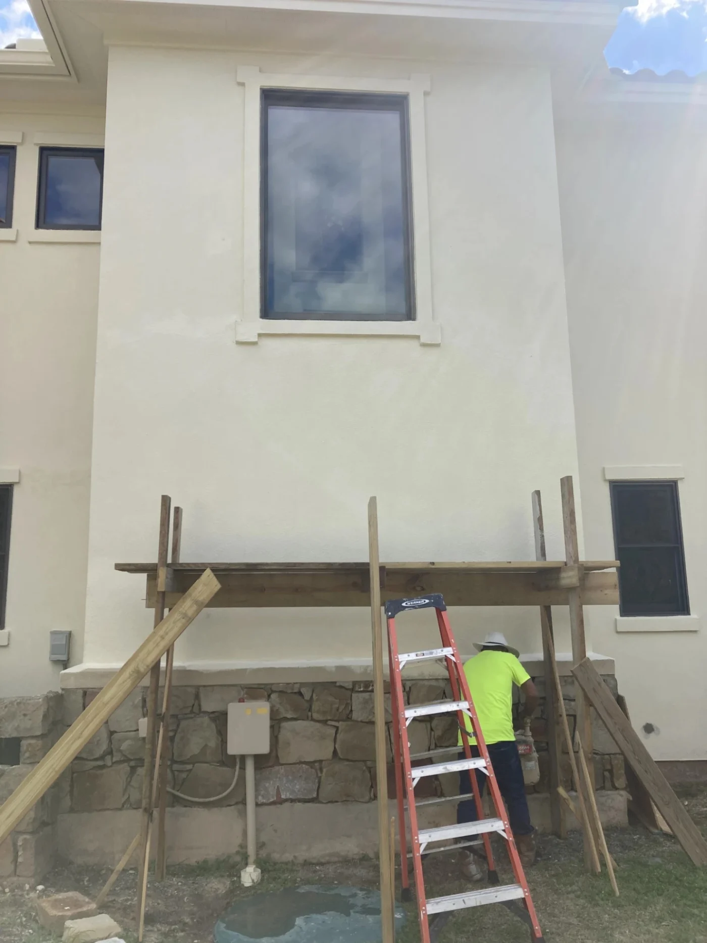 A worker sets up scaffolding and a stepladder along a residential stucco wall to complete professional home exterior services.