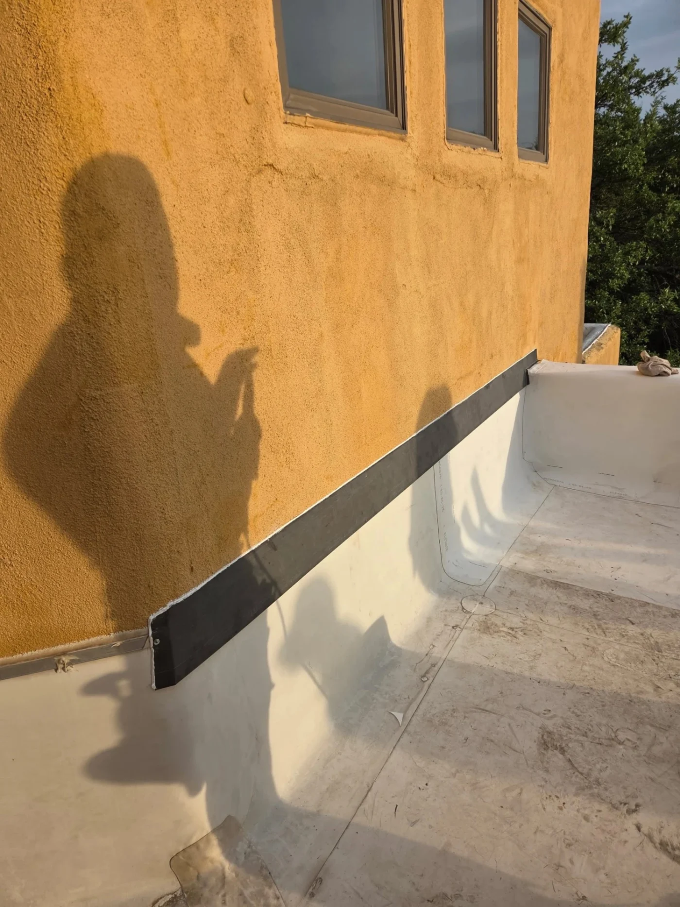 A flat roof membrane installation meets an orange stucco wall where sealing flashing is applied during professional home exterior services.