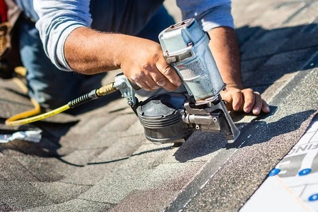 A contractor utilizes a pneumatic nail gun to carefully install new asphalt shingles during professional roof repair services.