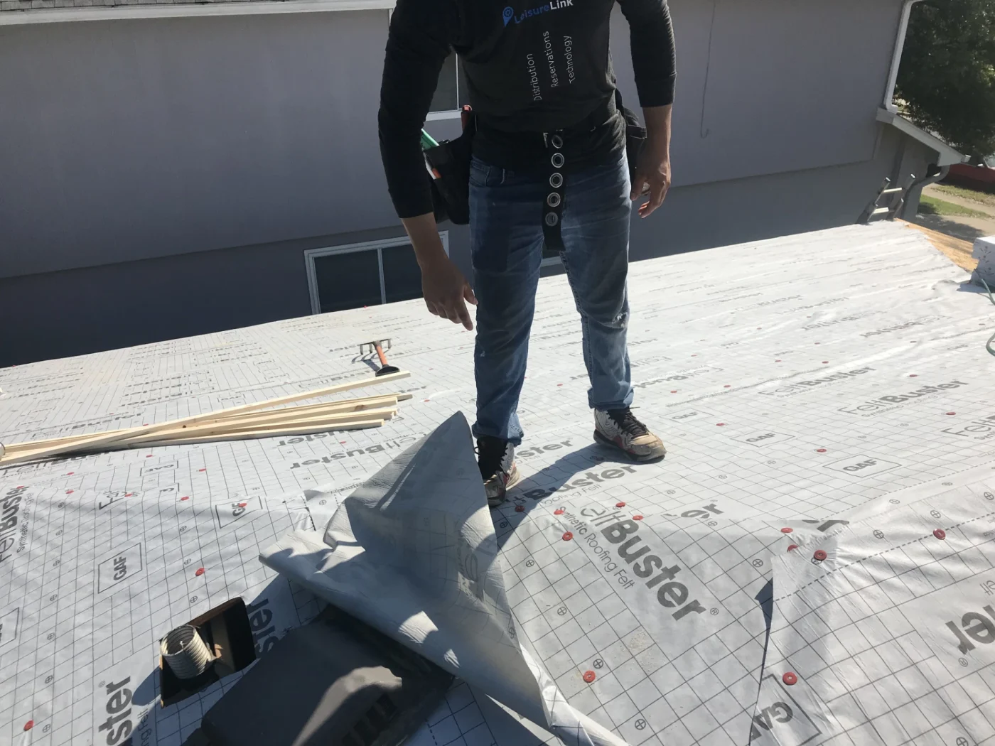 A contractor stands on a residential roof deck to install protective synthetic underlayment during a comprehensive roof replacement project.