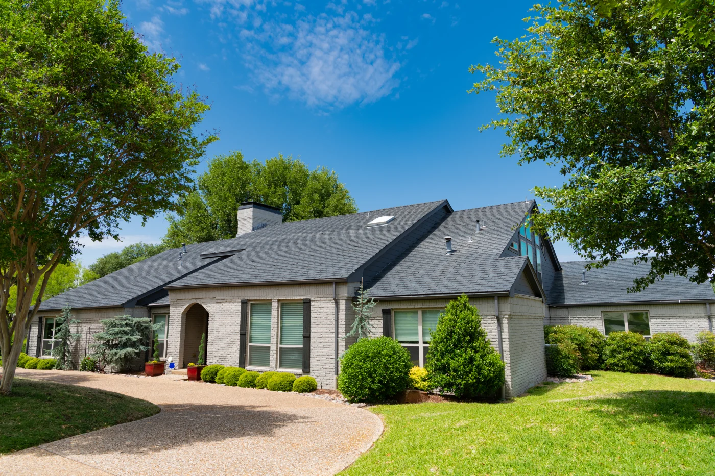 A brick house with white windows, black shutters, and a shingle roof.