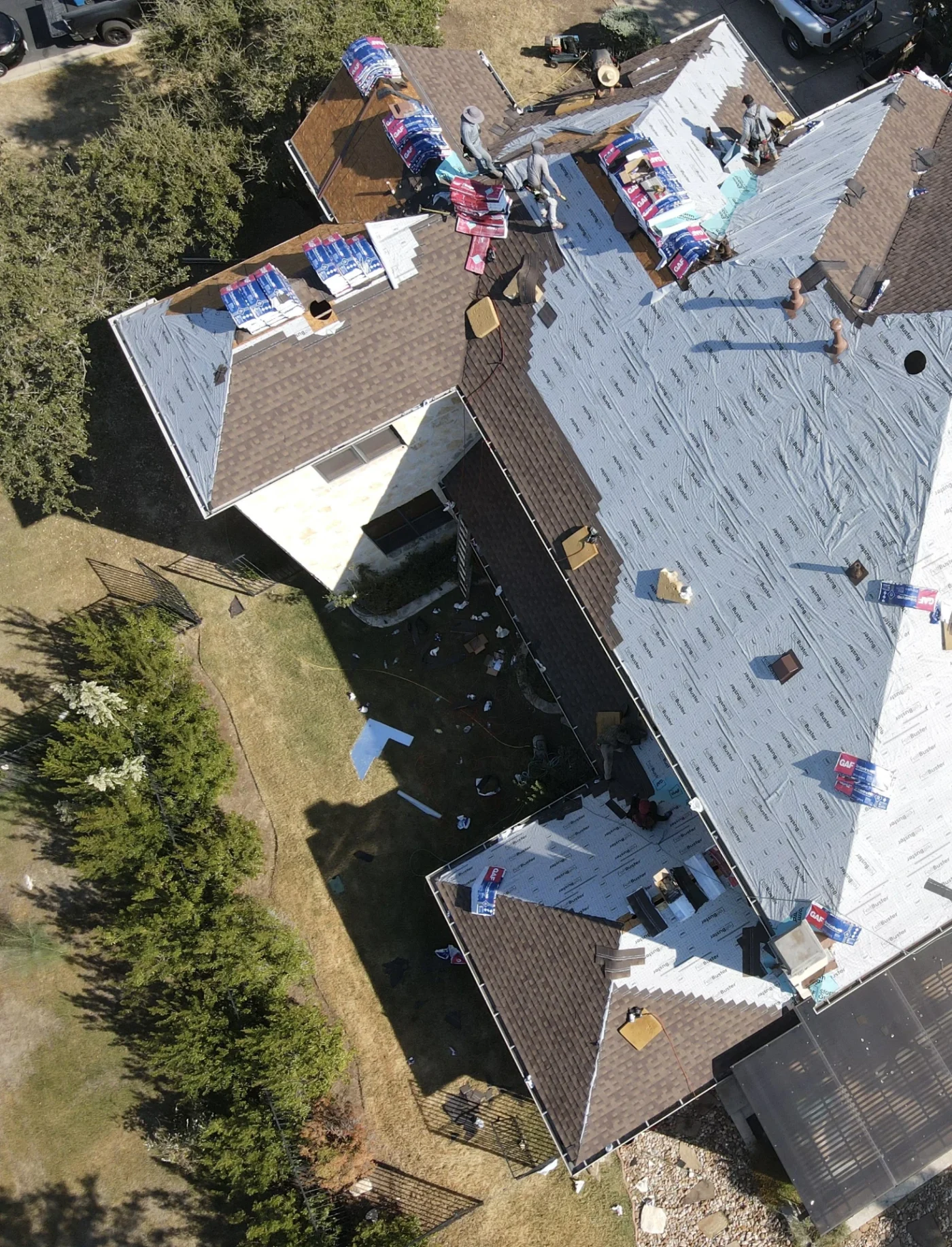 An aerial view of roofers replacing the asphalt shingle roof of a white house.