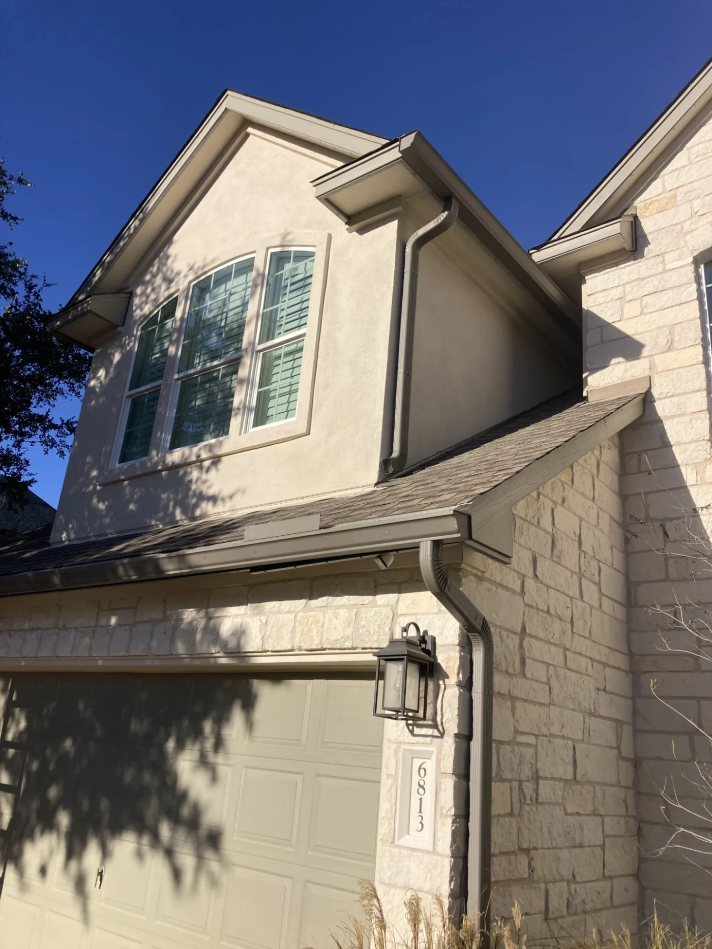A stone and stucco house with a brown garage, white windows, and an asphalt shingle roof.