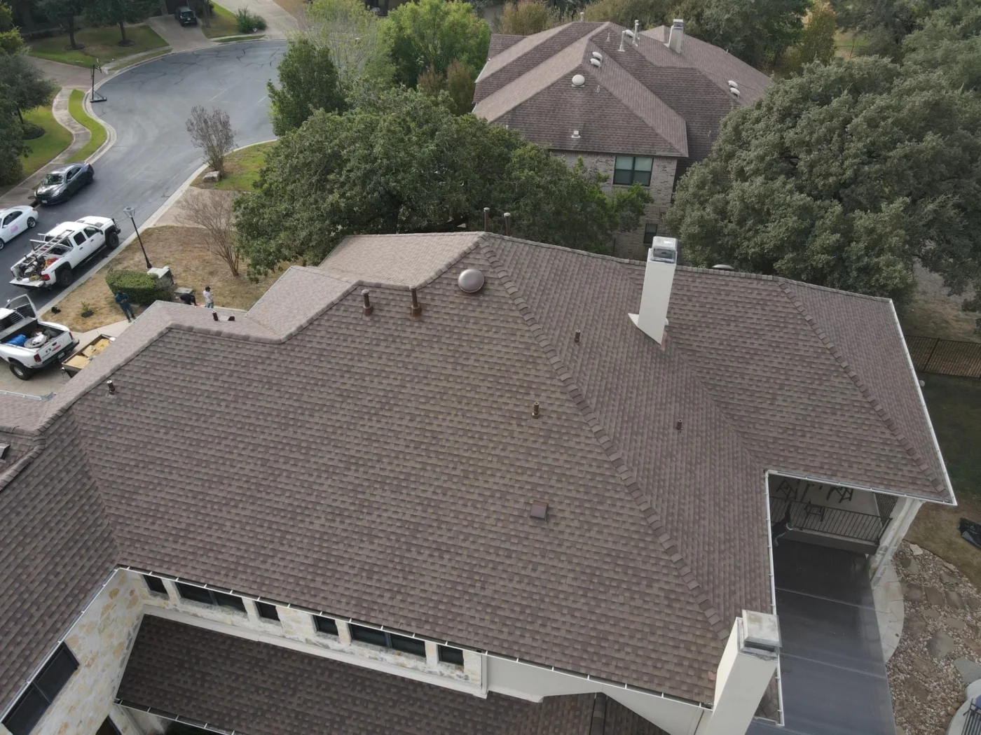 An aerial viewpoint showcases a complex, multi-gabled residential roof freshly finished with premium brown asphalt shingles that demonstrate top-tier roofing services.