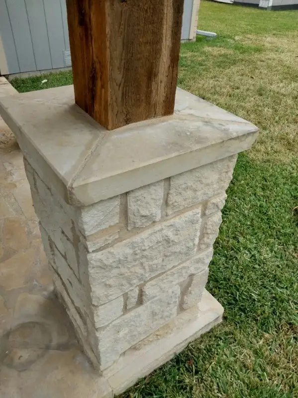 A close-up view of a stone base with a wooden post in front of a gray house.
