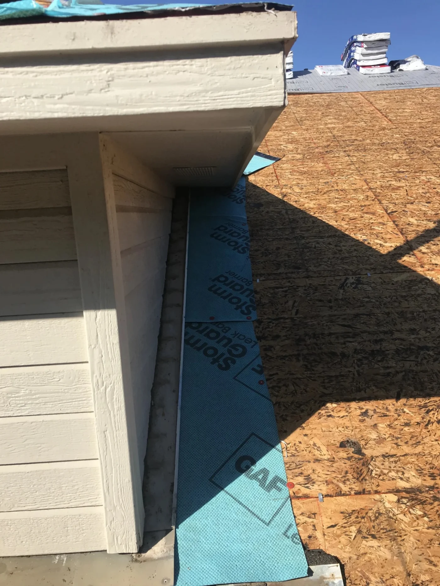 A protective blue leak barrier is installed along the roof deck valley next to the siding, prepping the home for a full roof replacement.