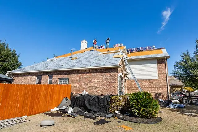 A side view of roofers replacing the roof on a brick house.