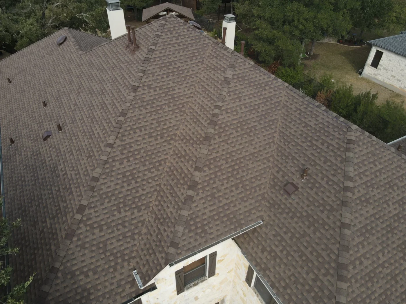 A close-up aerial view of an asphalt shingle roof on a stone house.