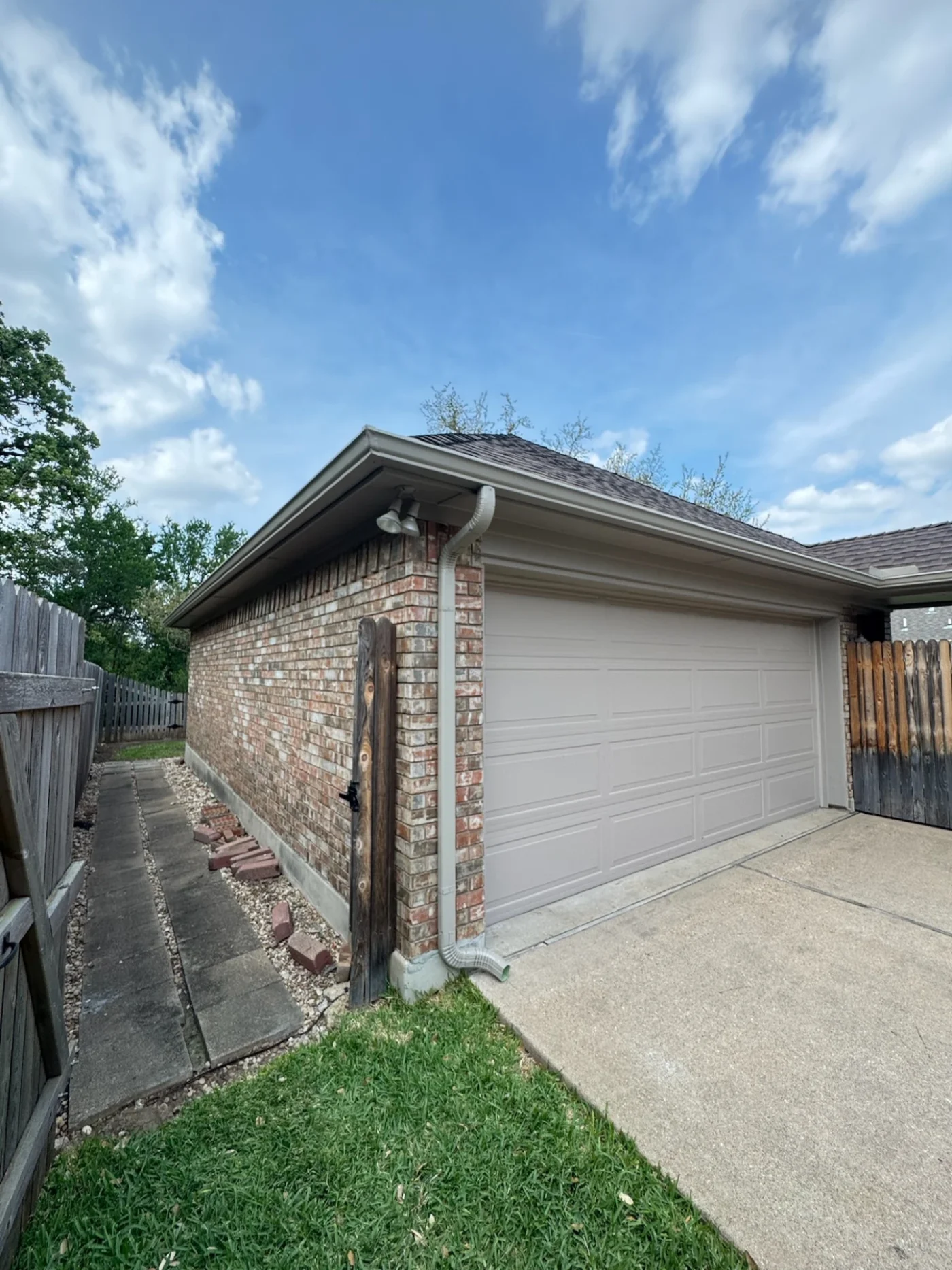 The corner of a brick house with a gray garage door, gray gutters, and a gray downspout.