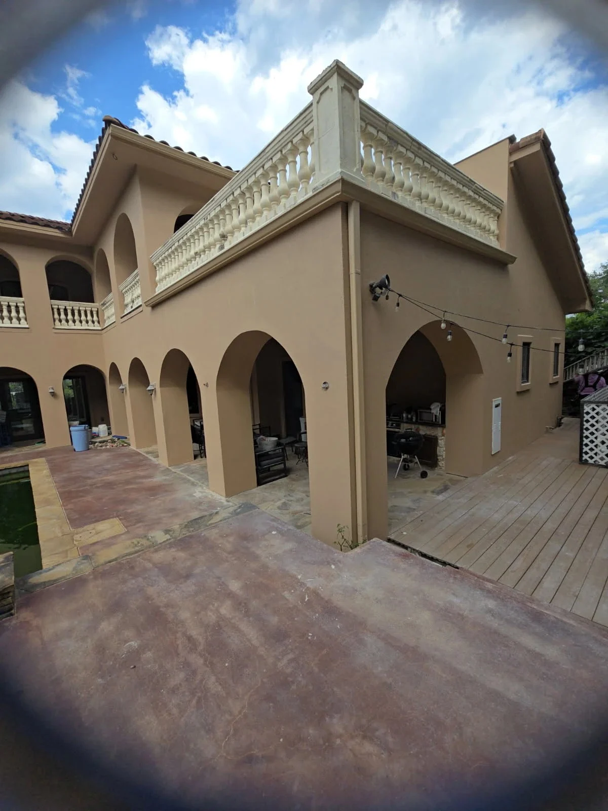 The expansive patio area features a large stucco home with arched entryways and a detailed stone balustrade balcony that's been beautifully restored with professional masonry repair services.