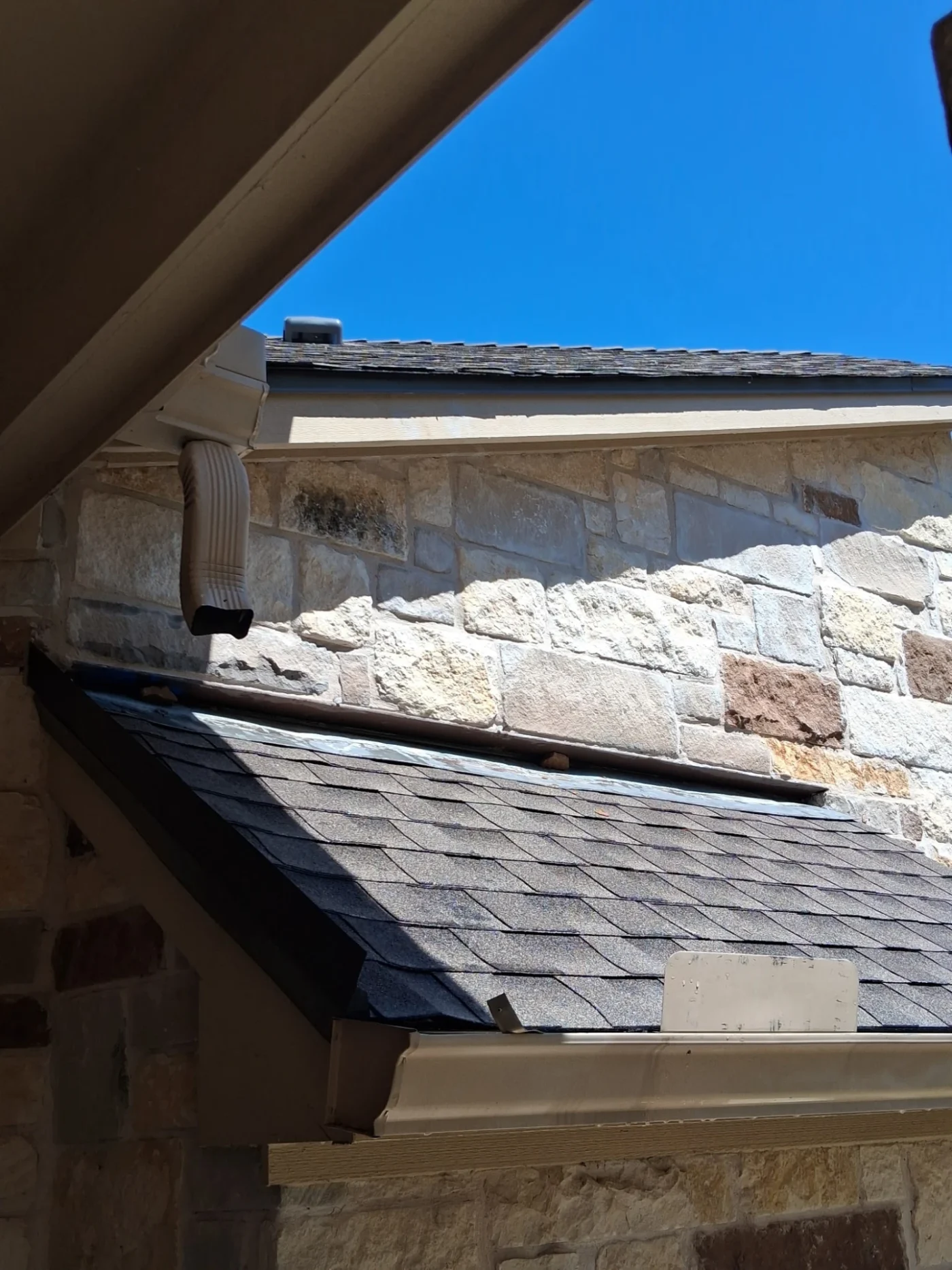 A close-up view of a stone house with an asphalt shingle roof.
