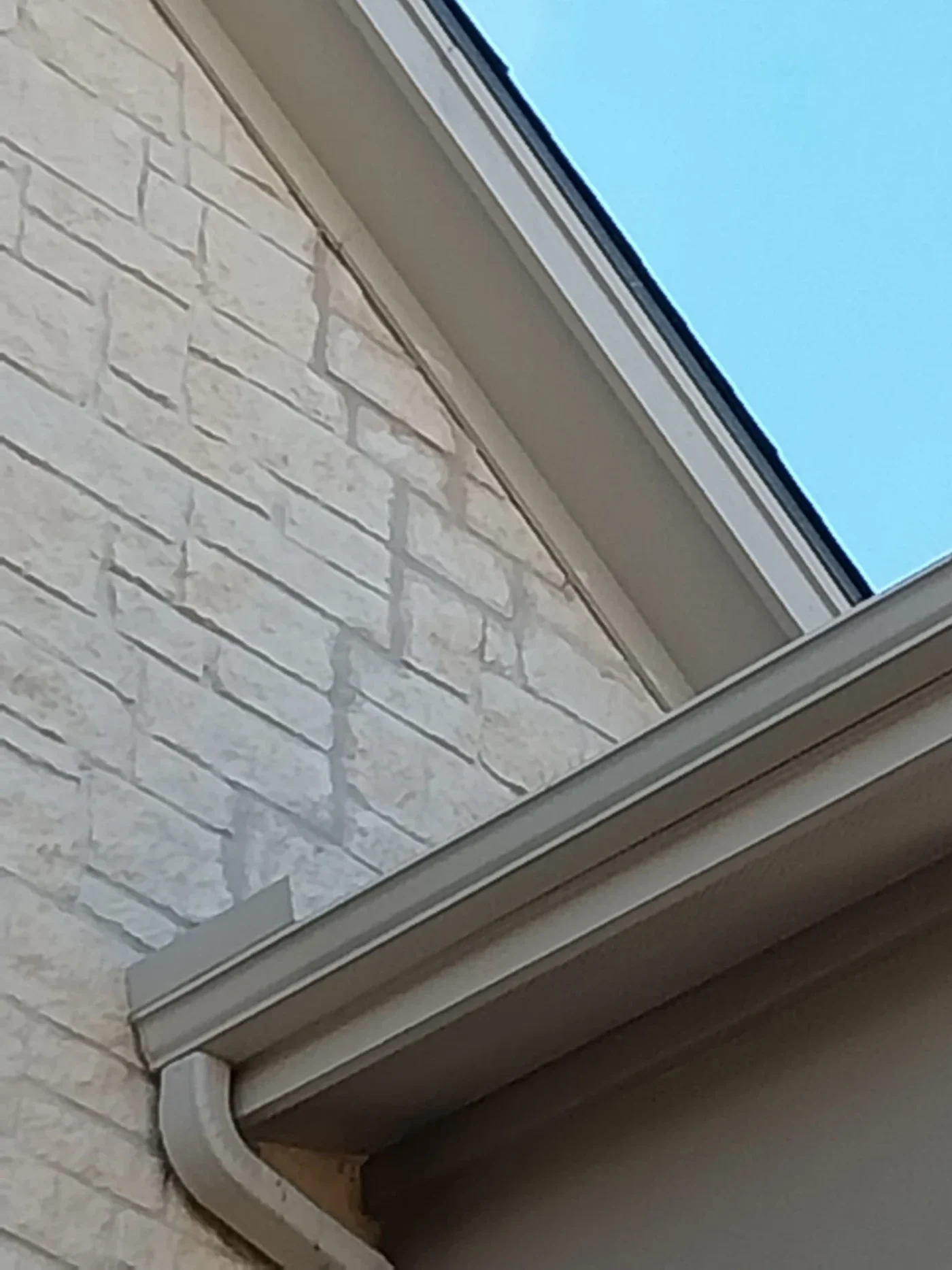 A close-up view of a stone house with white gutters and a white downspout.