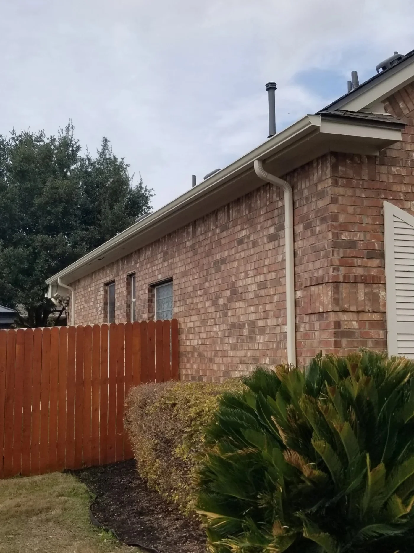 A seamless white gutter and downspout are neatly fitted along the roofline of a brick house, demonstrating professional home exterior services and quality gutter installation.