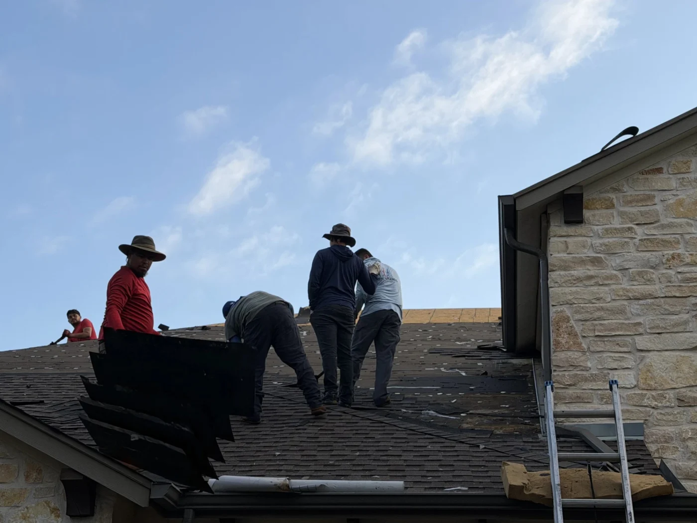 A team of contractors works together on top of a residential roof to tear away old shingles, showcasing the physical labor involved in a project managed by a professional roofing company.