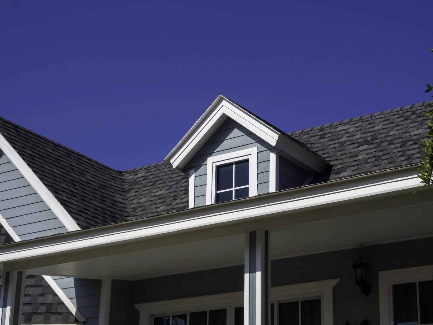 Durable Roofing Services In Belterra, TX | Wolfpack Roofing An upward view at a gray house with white windows, white trim, and an asphalt shingle roof.